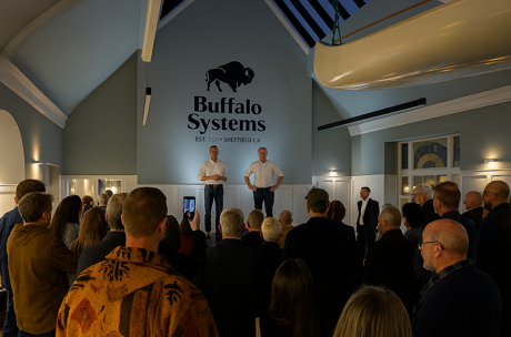 Indoor gathering in a room with distinctive architecture. People standing and facing a stage area